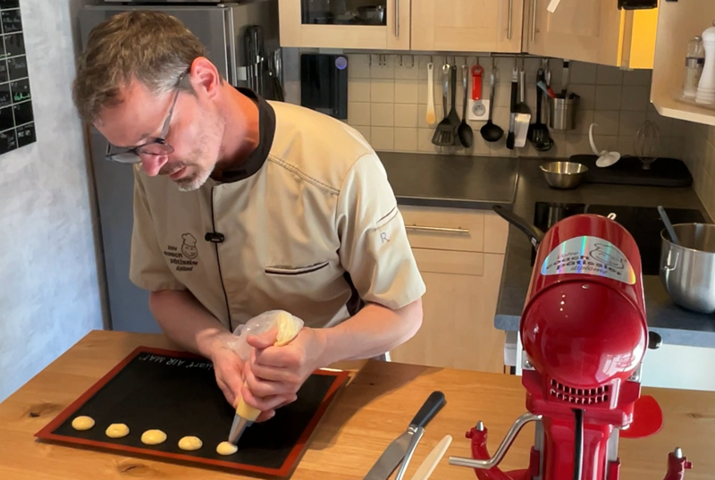 Formateur en pâtisserie démontrant la technique de pochage de choux lors d'une préparation au CAP Pâtissier